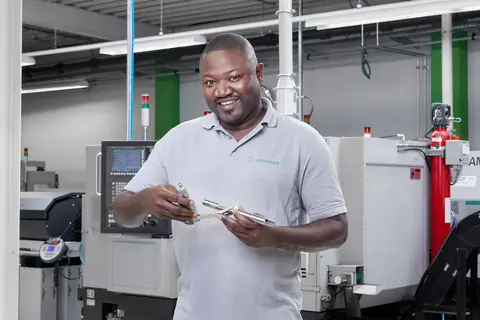 CNC-Fachkraft mit gefertigtem Instrument vor dem Maschinenpark